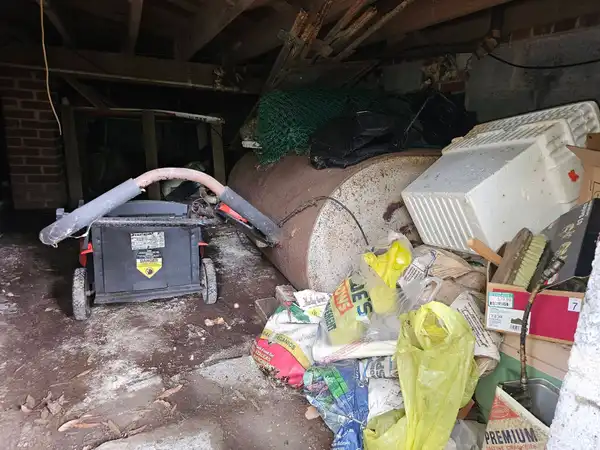 Bags, bulky household items and debris beside a tank in a crawl space