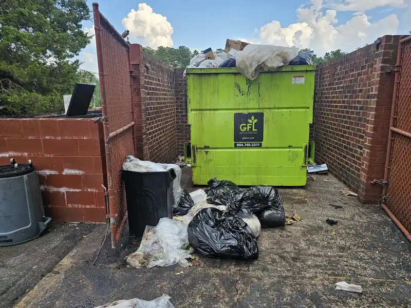 A dumpster enclosure overflowing with bagged trash and loose debris