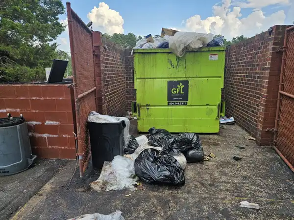 A dumpster enclosure overflowing with bagged trash and loose debris