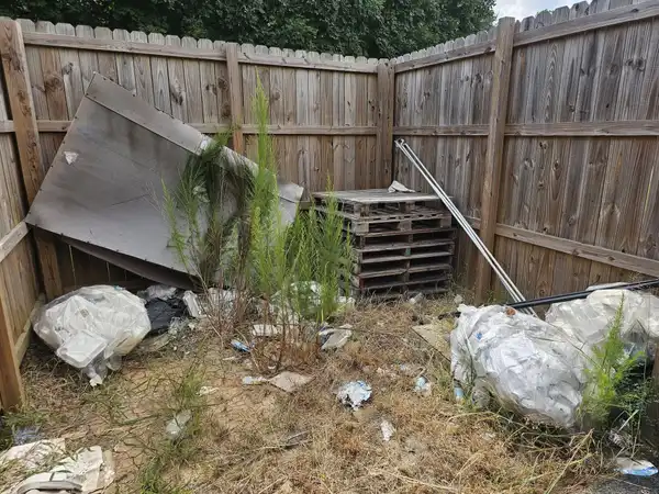 Pallets, boards and bagged debris piled in a wooden fenced corner