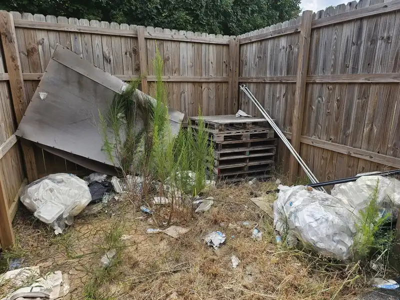 Pallets, boards and bagged debris piled in a wooden fenced corner