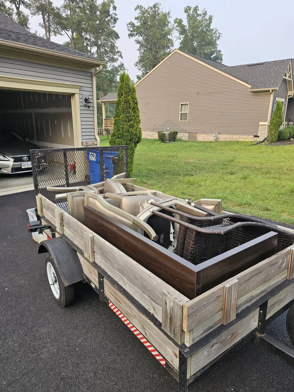 A loaded utility trailer parked in a driveway beside an open garage