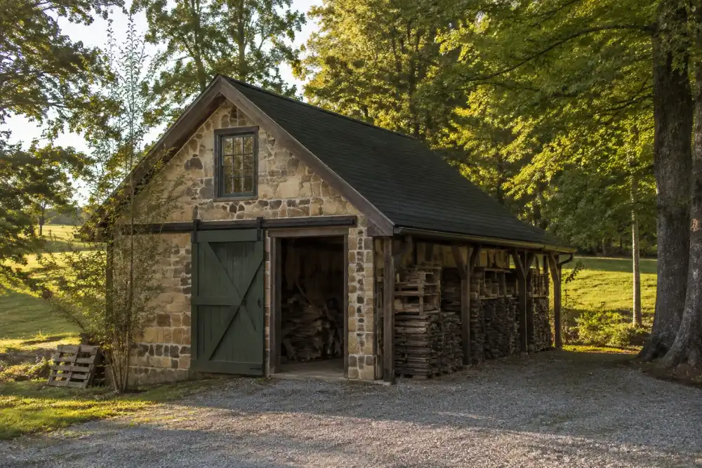Illustrative scene: goochland-inspired country property with a stone-and-timber outbuilding, rolling green pasture and gravel drive, neatly stacked scrap wood and old shelving