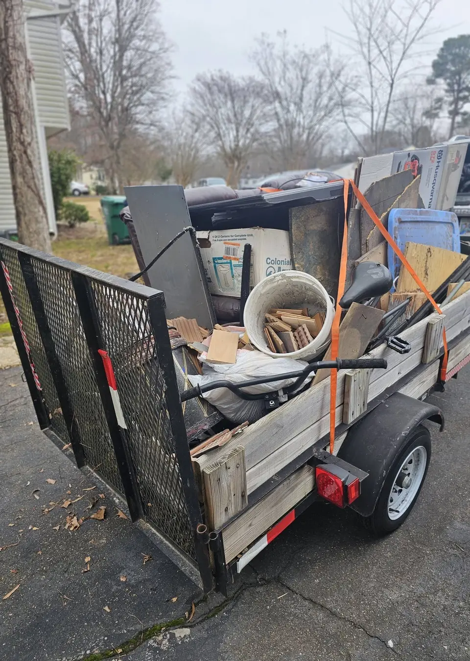 A utility trailer carrying bulky household items and a coiled hose