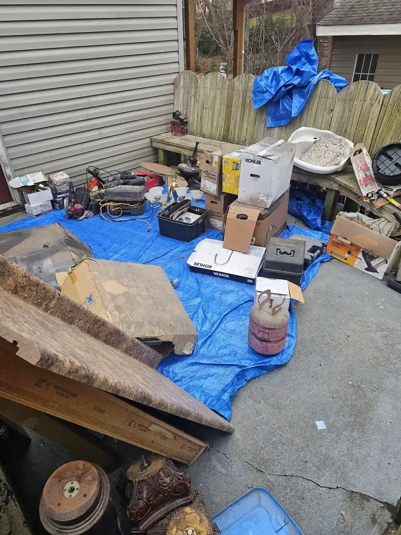 Boxes, containers and bulky items piled on a tarp beside a patio fence