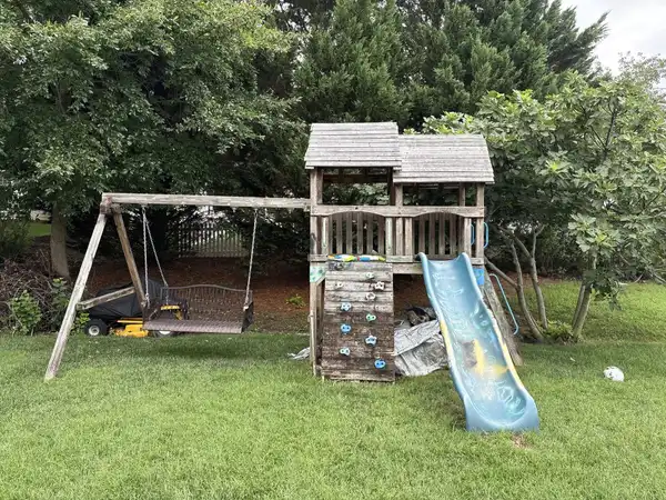An old wooden playset in a fenced backyard