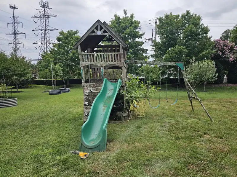 A wooden playset with a tower and slide on an open lawn