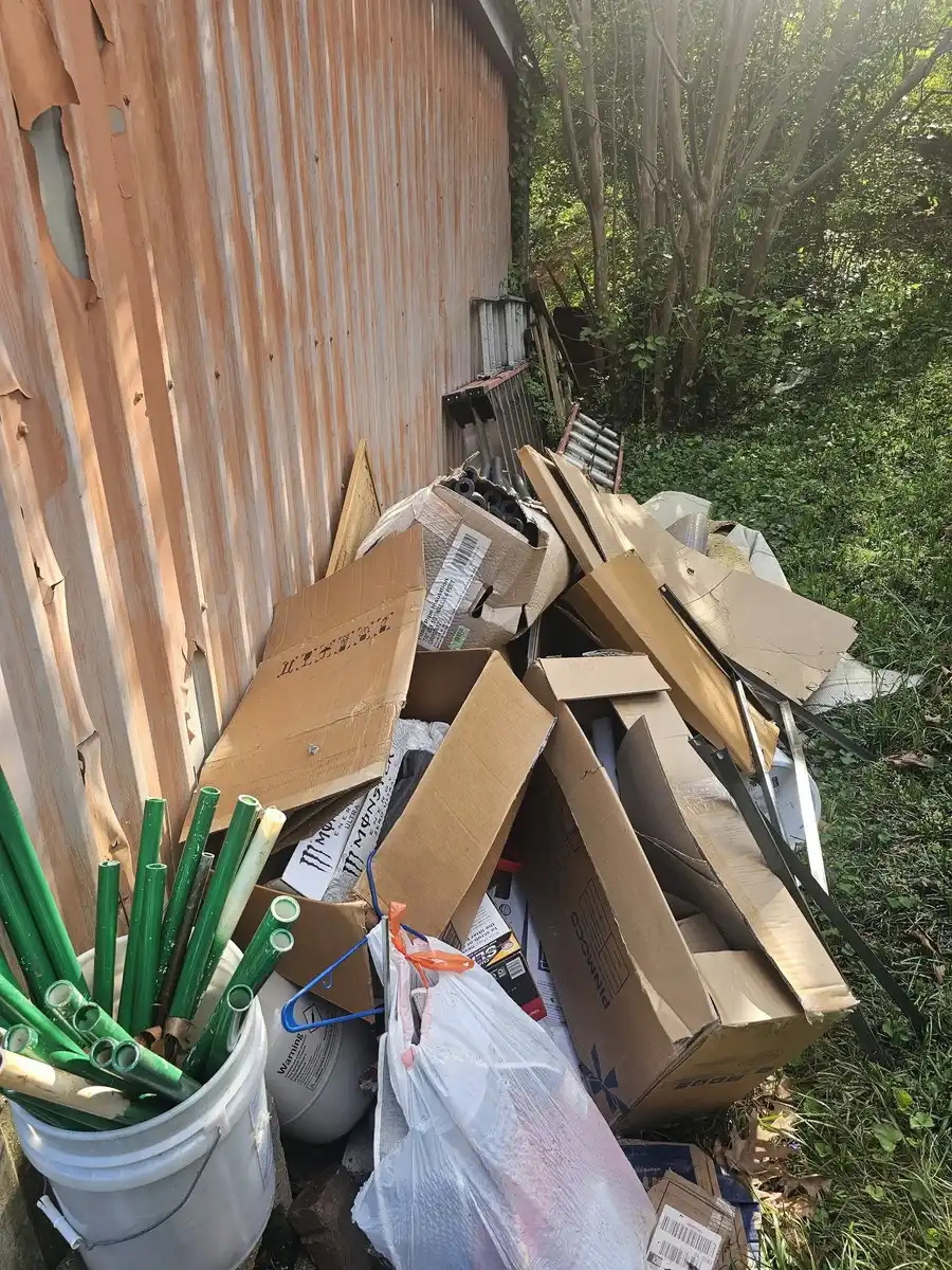 Cardboard, lumber and household debris piled against a metal shed
