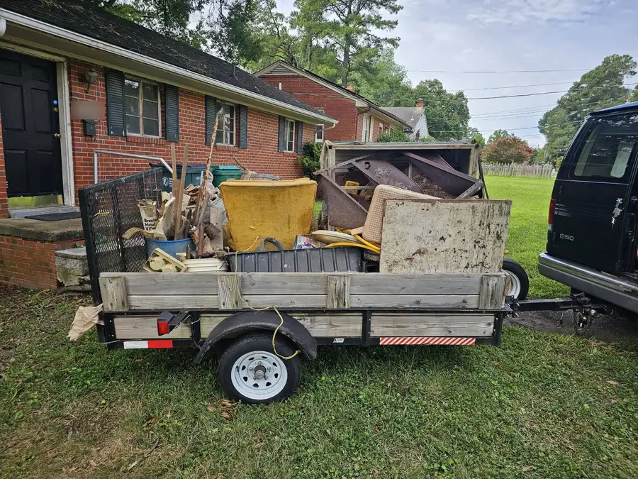 The Salem Junk Removal trailer loaded with a couch, chairs and boxes in front of a brick house in Richmond
