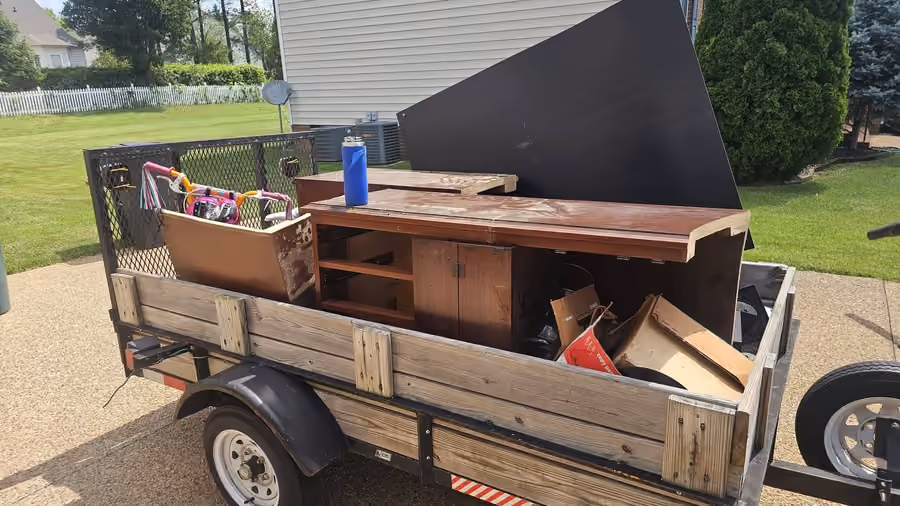 A utility trailer loaded with wooden furniture and household items